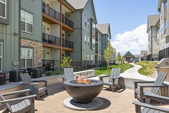 A fire pit sits in the middle of a patio surrounded by chairs.